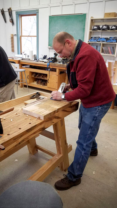 Student using a smoothing plane on a Moravian workbench in a woodworking class