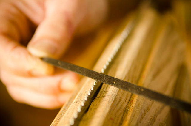 Triangular file sharpening hand saw teeth in a woodworking workbench vise