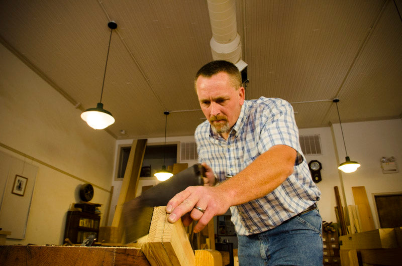 Will Myers using a woodworking hand saw to cut the legs of a Moravian workbench