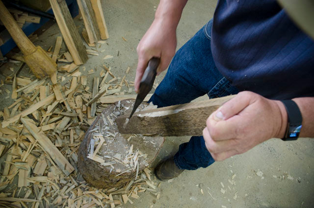 Woodworker shaping a shaving horse leg with a hatchet at a woodworking class
