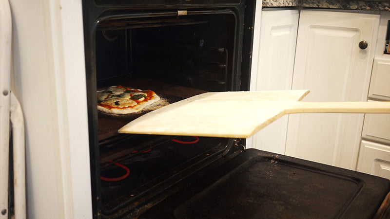 Pulling cooked pizza from an oven with a wooden pizza peel