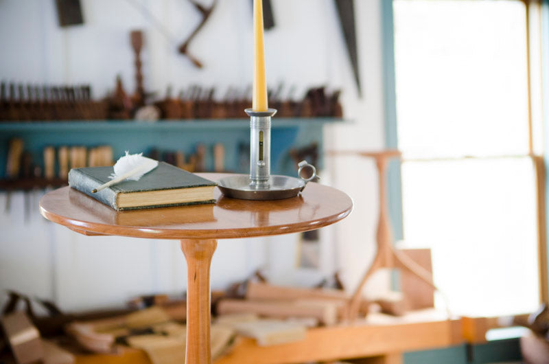 Hancock shaker candle stand with candlestick, book, and woodworking hand tools in the background