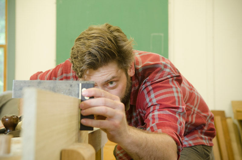 Man using a try square on a board in a hand tool woodworking class