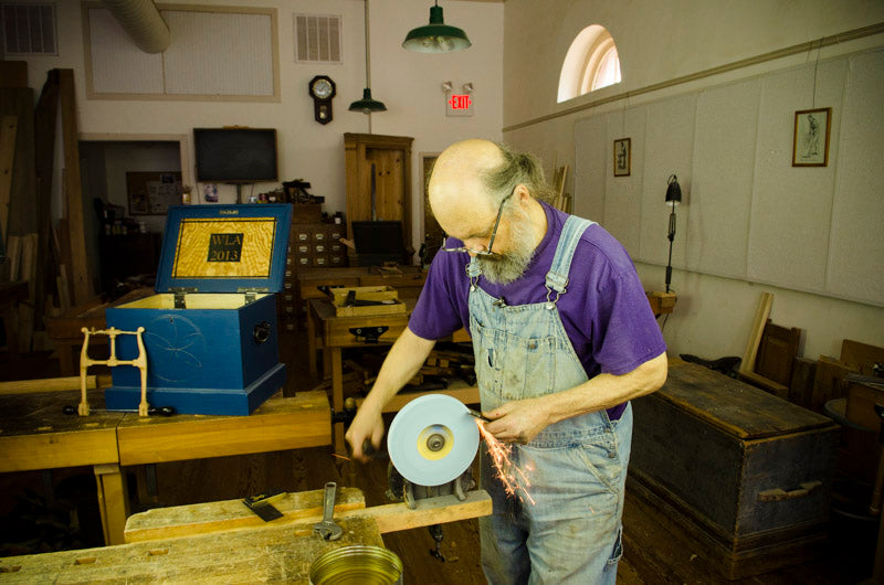Bill Anderson using a hand crank grinder to sharpen a hand plane blade