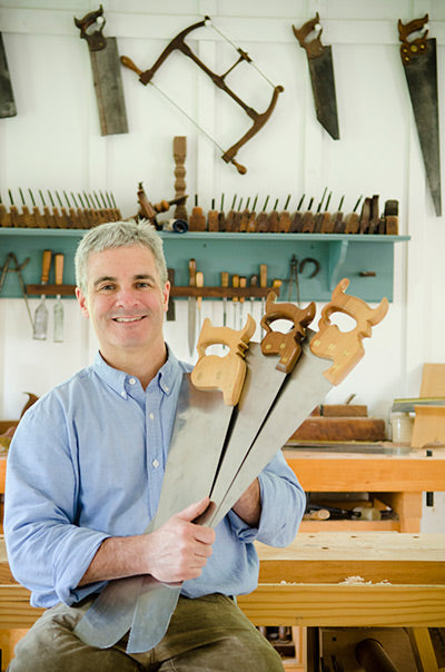 Woodworker Tom Calisto holding three hand saws in a woodworking workshop