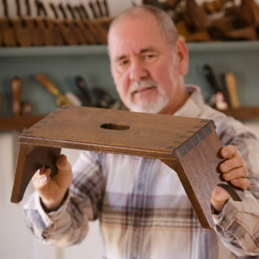 David Ray Pine looking at a dovetailed Moravian footstool in a woodworking school