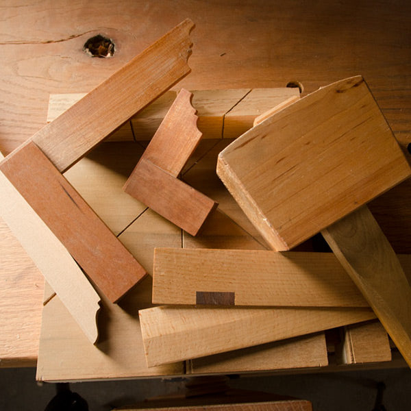 Woodworking hand tools sitting on a workbench including joiner's mallet, wooden try squares, winding sticks, wooden straight edge, and a miter bench hook