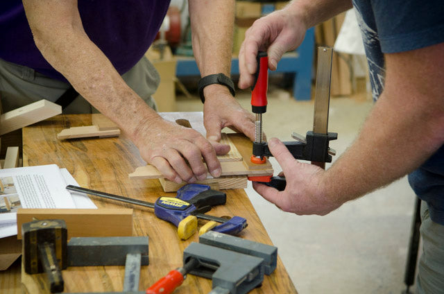 Woodworkers in a hand tool woodworking calss gluing up a wooden try square with wood clamps