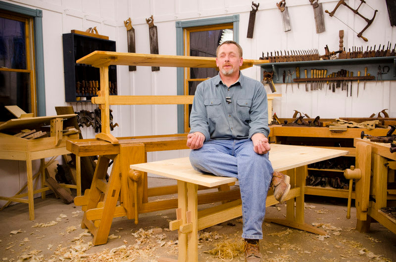 Will Myers Sitting On The Finished Trestle Table In A Funny Zen Position Next To Woodworking Workbenches In Joshua Farnsworth'S Woodworking Workshop